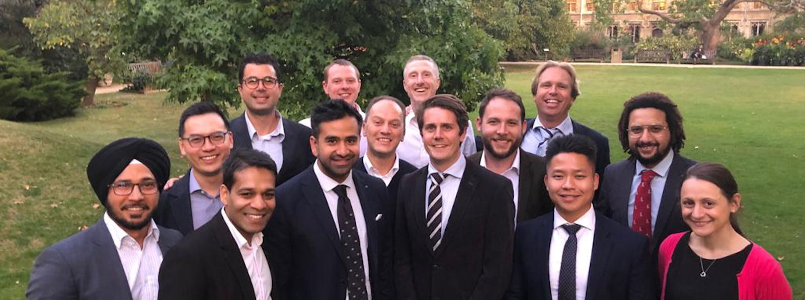 13 young men and one young woman, smartly dressed, smiling in a garden