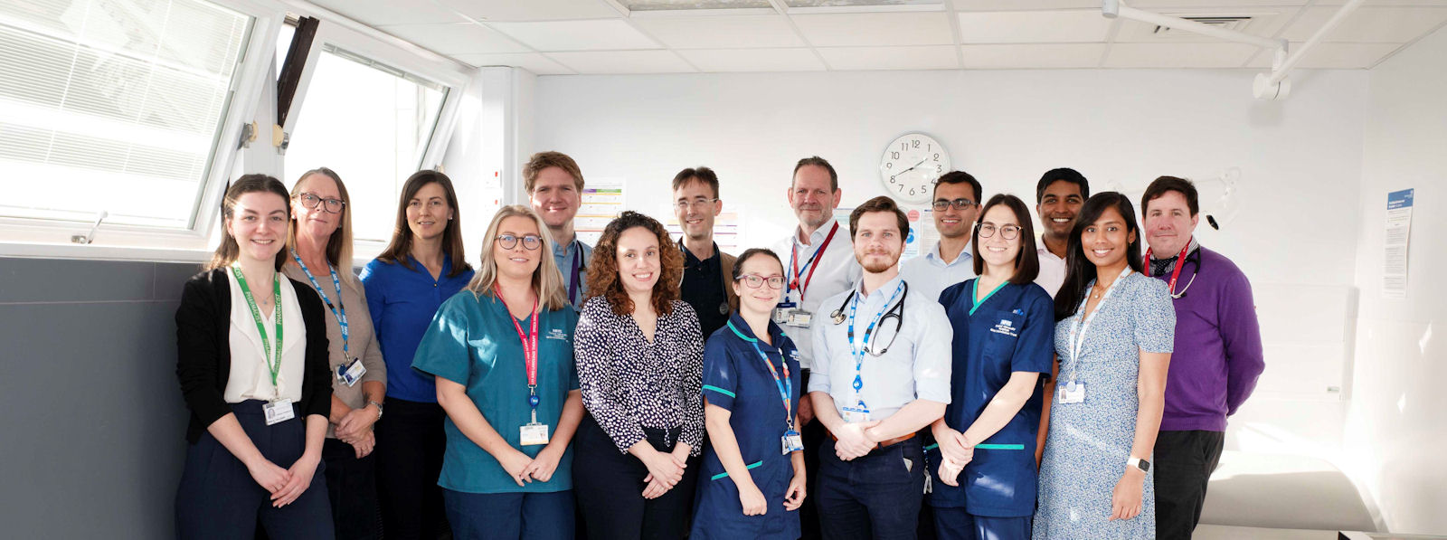 15 smiling people wearing lanyards, some in healthcare worker uniforms
