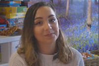 Young woman in bright communal room with boxed games on shelf behind