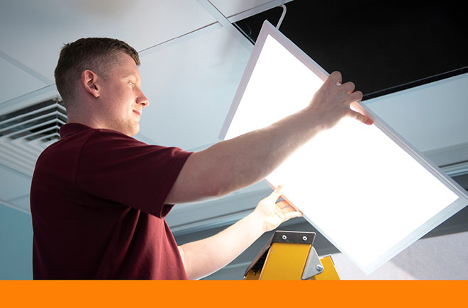 Man at top of step ladder carefully holds lighted panel up to gap in ceiling