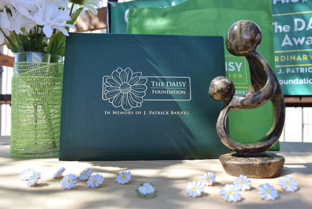 White flowers, small statuette and folders labelled 'The DAISY Foundation' on a sunny table